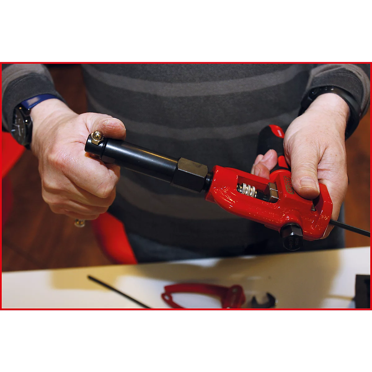 Person hält ein rotes Werkzeug, das Metallrohre verbindet. Das Werkzeug ist in Detailansicht.